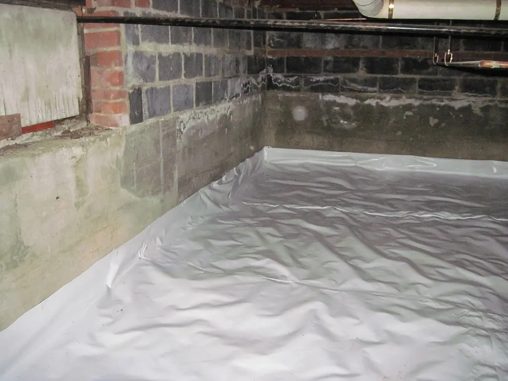 Cleared crawl space with a white vapor barrier over the ground