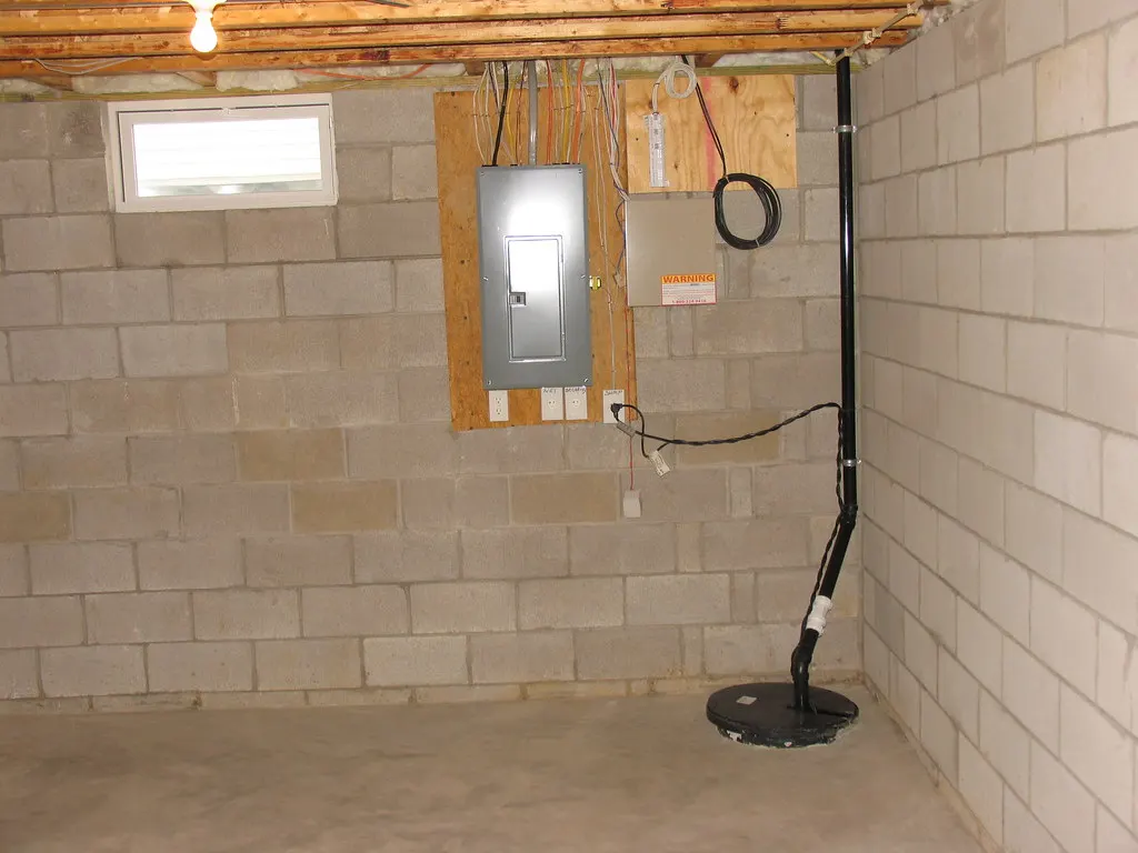 Sump pump installed in a pit beside a block wall